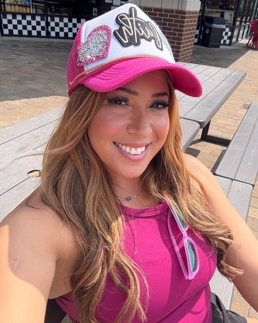 Angela Elgani smiling in a pink trucker hat and pink tank top